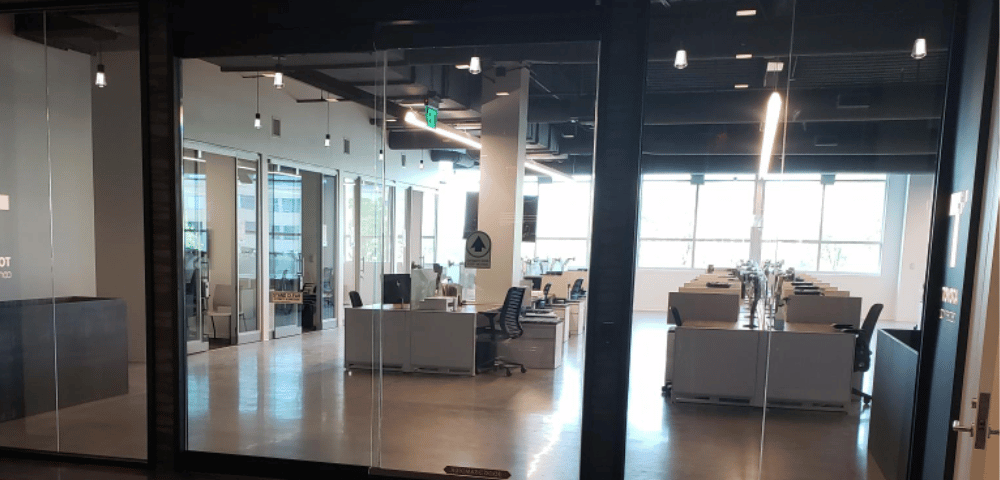 Modern office space with glass walls, multiple desks with computers, ergonomic chairs, bright overhead lighting, and reliable commercial doors supported by regular automatic door maintenance.