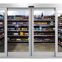 A glass-door fridge, seamlessly maintained by commercial door repair specialists, displays rows of assorted bottled beverages, primarily beer, arranged on shelves inside a store.