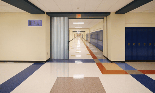 Empty school hallway with colorful tiled floor, blue lockers on the right, and a sign labeled "Drama" above a doorway on the left, showcasing the need for reliable automatic door maintenance in busy educational settings.